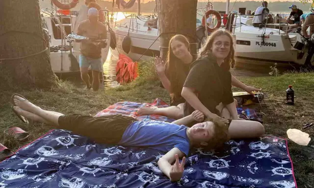 Relaks na kocyku z morskim motywem podczas długiego weekendu czerwiec 2026. W tle łodzie i zachód słońca.