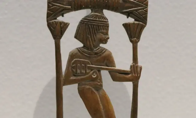 Sculpture en bois d'un musicien égyptien jouant d'un instrument ancien, ornée de motifs floraux.