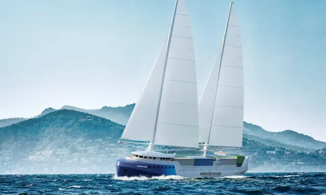 Un porte-conteneurs à voile futuriste navigue sur une mer agitée, avec des montagnes verdoyantes en arrière-plan.