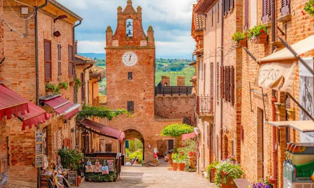 Un vicolo pittoresco a Gradara e dintorni, con case in mattoni, negozietti e un'antica torre dell'orologio.