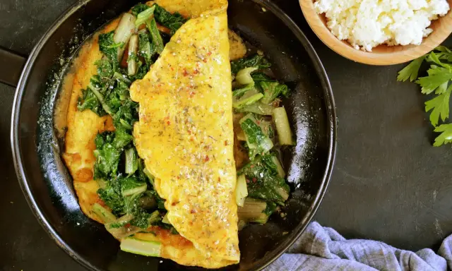 Pyszny omlet na słono z zielonymi warzywami, doprawiony ziołami. Obok miseczka białego sera i natka pietruszki.