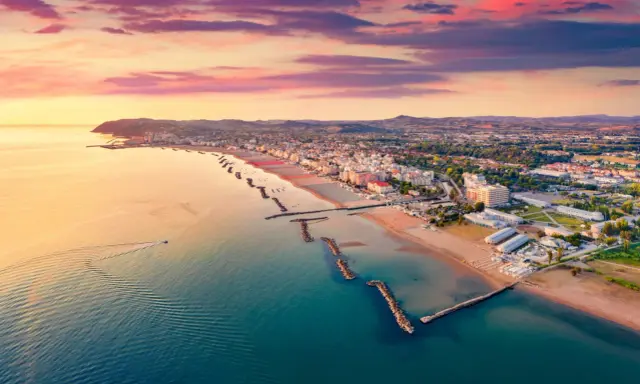 Alba rosata sul porto di Cattolica, con la costa e le spiagge dorate che si estendono verso l'orizzonte.