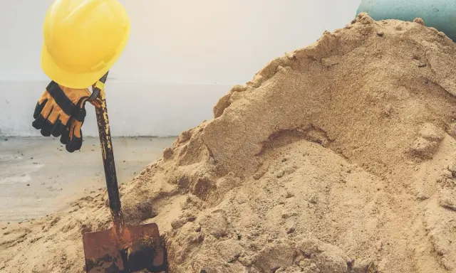 Żółty kask i rękawice na łopacie, obok sterty piachu. Zastanawiasz się, ile waży metr sześcienny piachu?