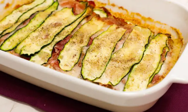 Sformato di zucchine appena sfornato, con fette sottili di zucchina grigliata, prosciutto e formaggio filante, condito con pepe nero.