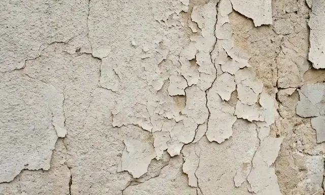 Texture d'un mur qui s'effrite, révélant des couches de peinture écaillée et des fissures profondes.