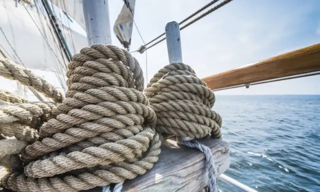 Gros cordages enroulés sur un voilier, prêts pour le moteur fonctionnement. La mer bleue et le ciel clair en arrière-plan.