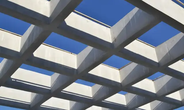 Estructura geométrica de vigas de hormigón armado, creando un patrón de cuadrados contra el cielo azul.