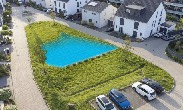 Eine blaue Fläche markiert eine geplante Mulde/Rigole in einem grünen Hang neben modernen Häusern und geparkten Autos.