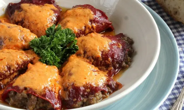 Pimientos rellenos de carne cubiertos con una cremosa salsa, decorados con perejil fresco.