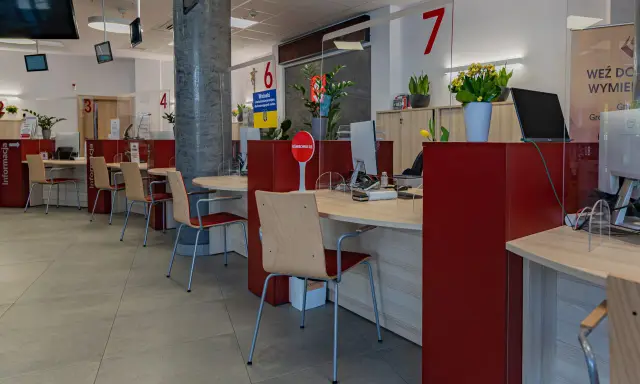 Puste biurka z krzesłami w urzędzie, gdzie przestrzegana jest proksemika. Widać numery stanowisk i tabliczki informacyjne.