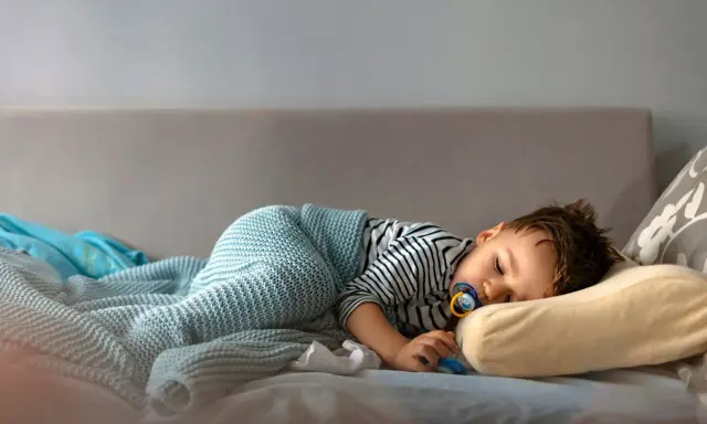 Mały chłopiec śpi na kanapie, otulony kocykiem. Wygląda na to, że mimo początkowego buntu, kiedy dziecko rezygnuje z drzemki, w końcu uległ zmęczeniu.