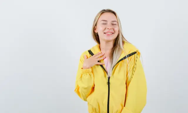 Uśmiechnięta blondynka w żółtej kurtce softshellowej, która przypomina jej, jak prać softshell, by zachować jego właściwości.