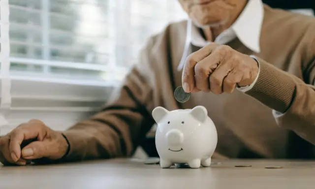 Un anciano deposita una moneda en una hucha, preparándose para la jubilación obligatoria.