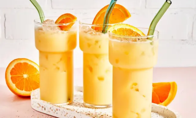 Drei cremige, eisgekühlte Painkiller Cocktails mit Orangenscheiben und grünen Strohhalmen auf einem Terrazzo-Tablett.