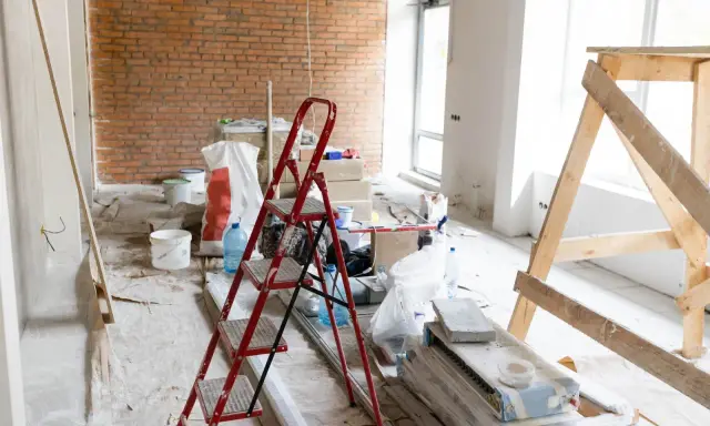 Remont w toku. Czym usunąć pył gipsowy? Na podłodze folia, drabina, wiadra, worki z materiałami budowlanymi i drewniane rusztowanie.