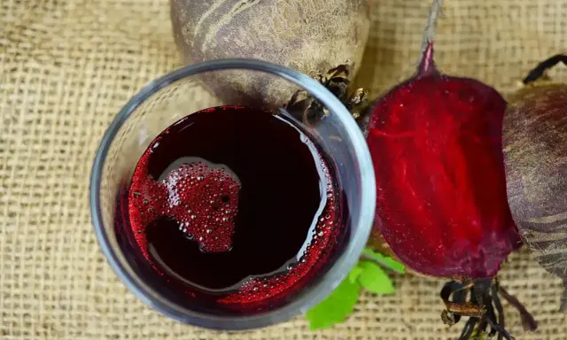 Verre de jus de betterave rouge vif, avec des betteraves entières et coupées autour. Une boisson saine pour savoir comment faire du jus de betterave.