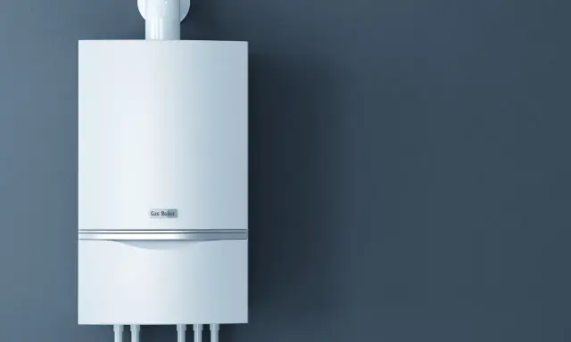 Nowoczesny piec gazowy 24kW na ile metrów zapewni ciepło? Biały, wiszący na ciemnoszarej ścianie, z widocznymi przyłączami.