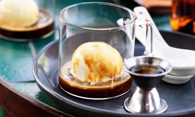 Ein cremiger Affogato mit Alkohol, serviert in einem Glas mit einer Kugel Vanilleeis, übergossen mit Espresso und einem kleinen Schnapsglas daneben.