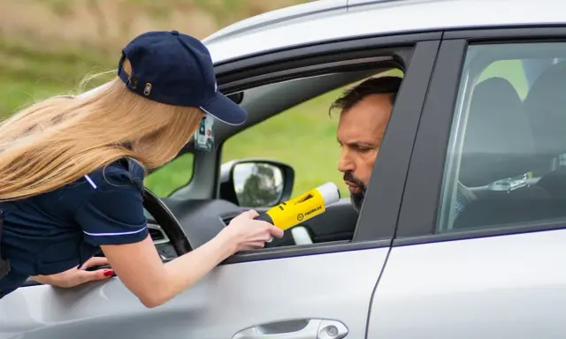 Policjantka mierzy kierowcy alkomatem, sprawdzając, czy nie przekroczył dopuszczalnego limitu promili.