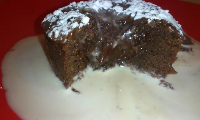Un fondant au chocolat dégoulinant, saupoudré de sucre glace, servi dans une sauce crémeuse sur une assiette rouge.