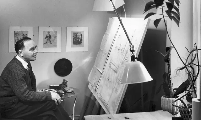 Paavo Tynell sitter vid sitt ritbord, omgiven av sina skisser och en stor ritning.