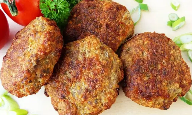 Cuatro filetes rusos dorados, listos para servir, acompañados de tomate, perejil y cebolleta.