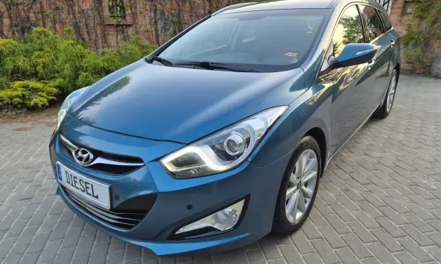Niebieski Hyundai i40 1.7 CRDi na podjeździe z kostki brukowej, z tyłu ceglany mur porośnięty bluszczem.