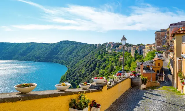 Widok na jezioro i zielone wzgórza z kolorowymi domami w Castel Gandolfo.