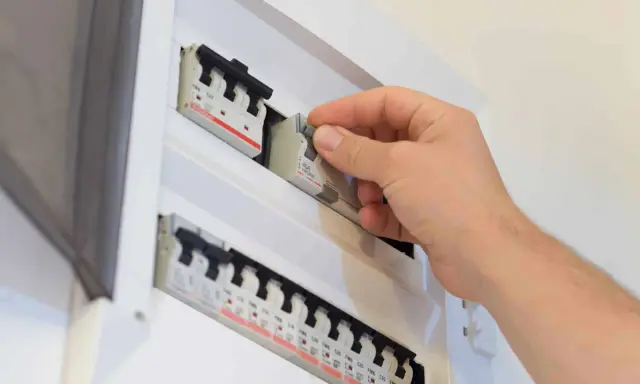Main disjoncteur général manipulé par une main dans un tableau électrique blanc.