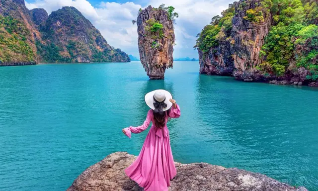 Donna con abito rosa e cappello bianco ammira la spettacolare **isola di James Bond** con le sue formazioni rocciose uniche e il mare turchese.