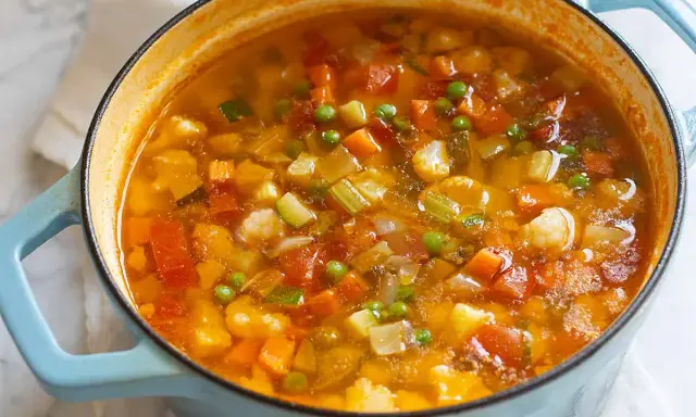 Un fumante minestrone di verdure in una pentola azzurra, ricco di carote, zucchine, piselli e pomodoro.