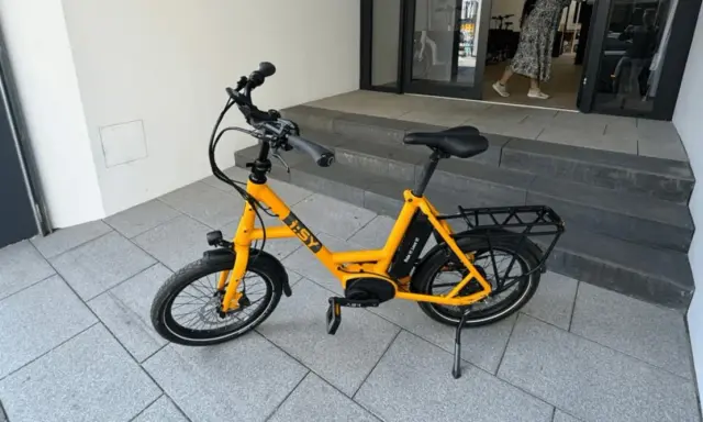 Gelbes i:SY E-Bike, das bei der Stiftung Warentest gut abgeschnitten hat, steht auf gepflastertem Untergrund vor einer Treppe.