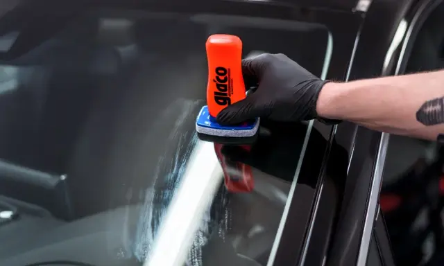 Rękawiczka z czarną rękawiczką nakłada preparat na szybę. To pokazuje, jak działa powłoka hydrofobowa, co to znaczy, że woda spływa.