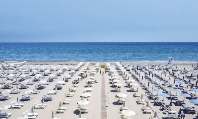 File di ombrelloni bianchi e lettini ordinati sui **stabilimenti balneari Cervia**, con il mare azzurro sullo sfondo.