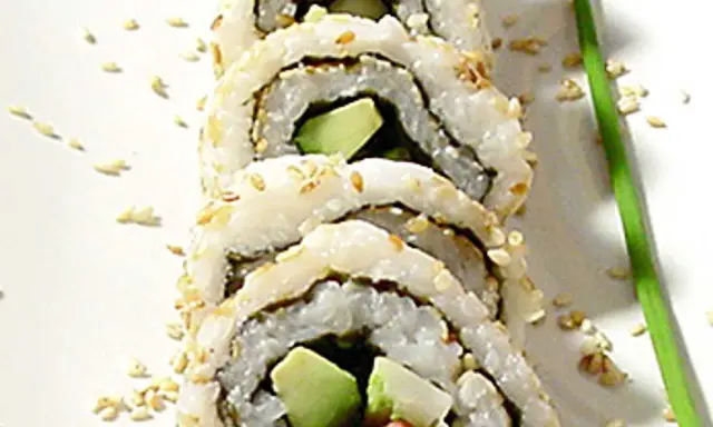 En närbild på en california roll med avokado och krabba, strödd med sesamfrön.