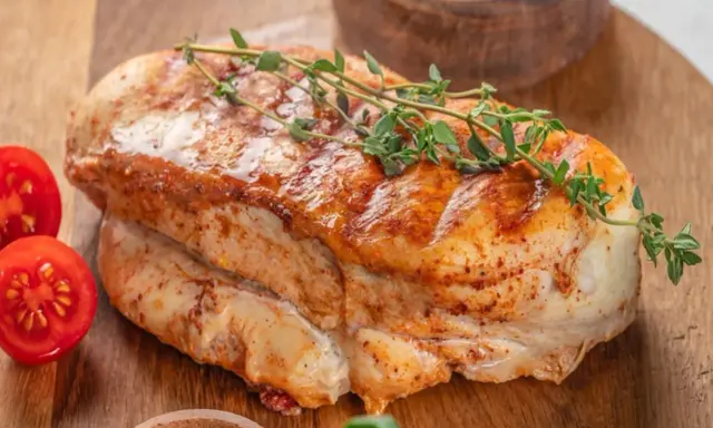 Soczysty filet z indyka, pieczony z ziołami, podany z pomidorkami koktajlowymi na drewnianej desce.