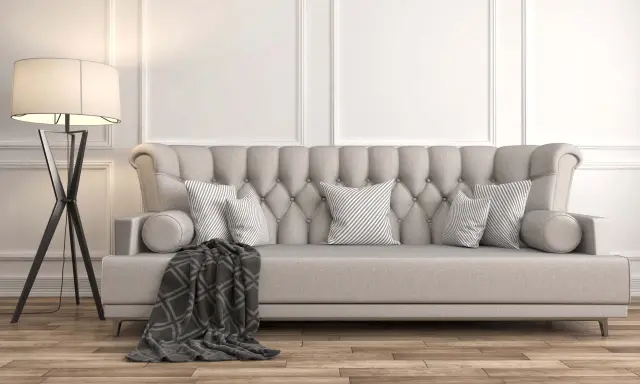 Divano imbottito grigio con cuscini a righe e coperta geometrica. La luce soffusa di una lampada da terra illumina la scena, dimostrando come grigio e beige stiano bene insieme.