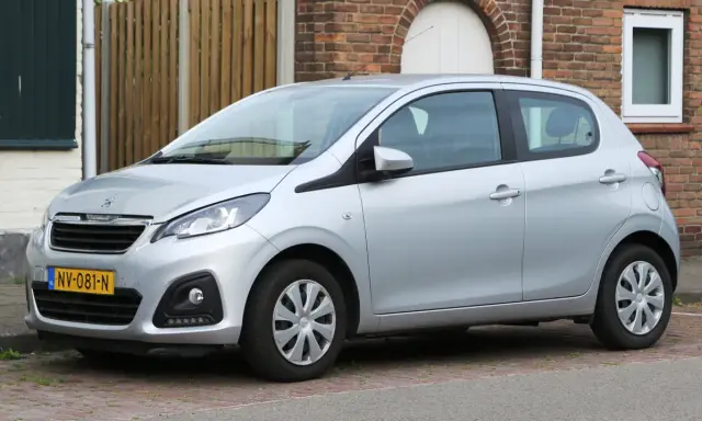 Srebrny Peugeot 108 stoi zaparkowany przed ceglanym domem.