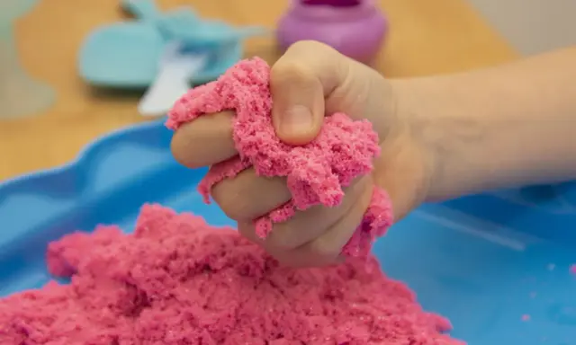 Kind hält pinken kinetischen Sand, der sich leicht formen lässt. Perfekt zum **kinetic sand selber machen** und Spielen.