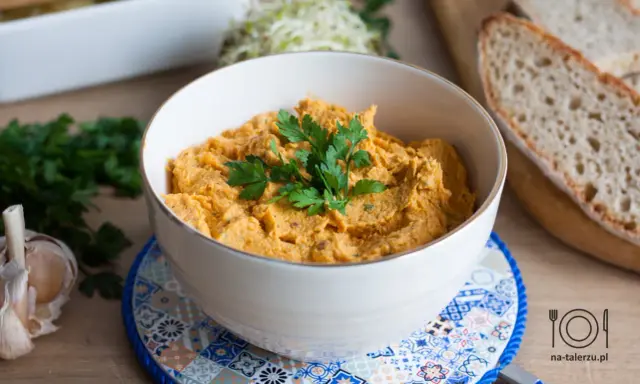 Pyszna pasta z kurczaka w miseczce, udekorowana natką pietruszki, obok czosnek i kromki chleba.