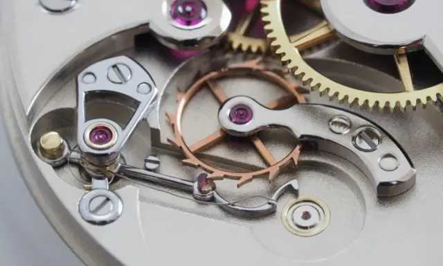 Meccanismo di orologio con ingranaggi dorati e ruota bilanciere, parte di uno scappamento coassiale.