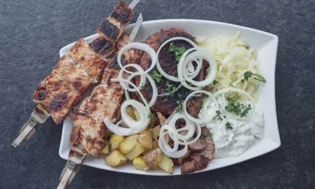 Ein Teller mit gegrilltem Fleisch, Kartoffeln und Krautsalat, garniert mit Zwiebelringen. Ein authentisches Souvlaki Rezept original.