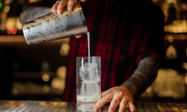 Barkeeper gießt einen erfrischenden Gin Fizz mit Eis in ein Glas.
