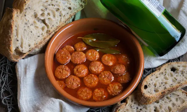 Chorizo a la sidra en cazuela de barro, acompañado de pan rústico y una botella de sidra verde.