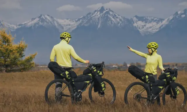 Para szykuje się na przygodę bike packing. W tle majestatyczne, ośnieżone góry.