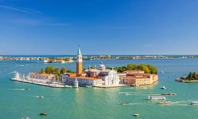 Vue aérienne de Venise, le campanile San Giorgio Maggiore se dresse fièrement sur son île, entouré d'eaux turquoise et de voiliers.