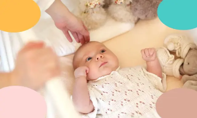 Un bebé despierto en su cuna, con una mano acariciándole la cabeza. Parece que mi bebe tarda mucho en dormirse.