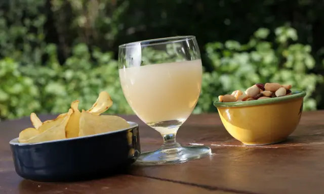 Verre de boisson claire, chips croustillantes et mélange de fruits secs, une spécialité PACA pour un apéritif ensoleillé.