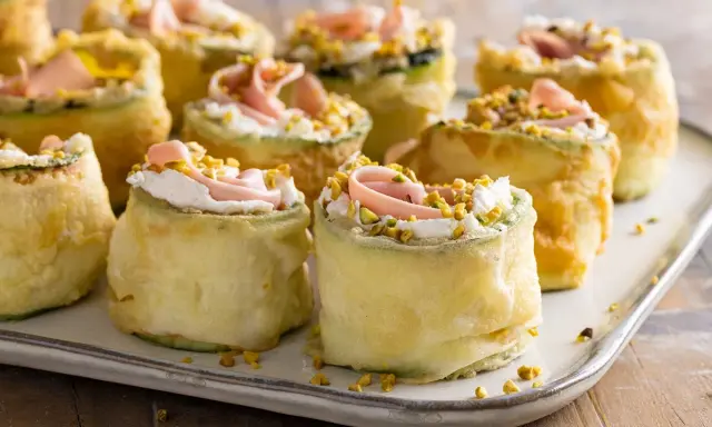 Rotolini di zucchine impanate e fritte, farciti con crema, prosciutto e pistacchi. Stuzzichini veloci ed economici perfetti per un aperitivo sfizioso.