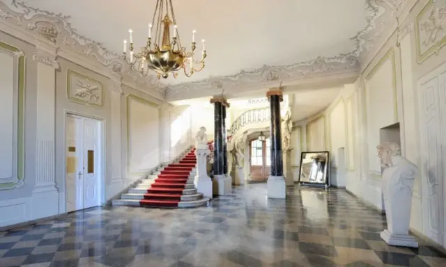 Elegancka klatka schodowa z czerwonym dywanem i żyrandolem w Pałacu Branickich w Białymstoku. Sprawdź cennik zwiedzania!